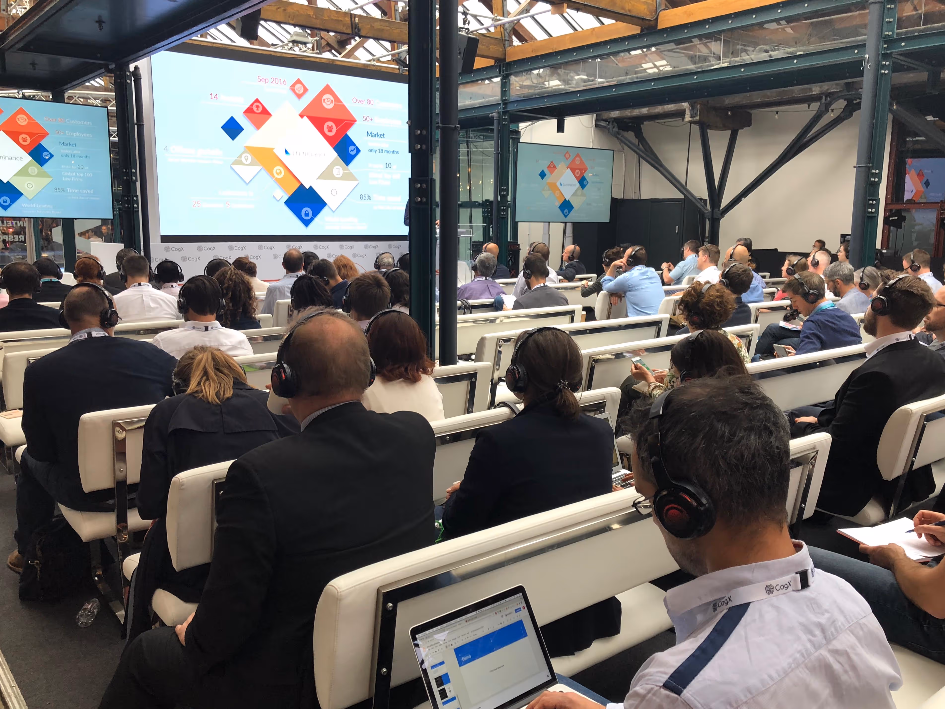 Conference attendees watching a presentation in a large hall.