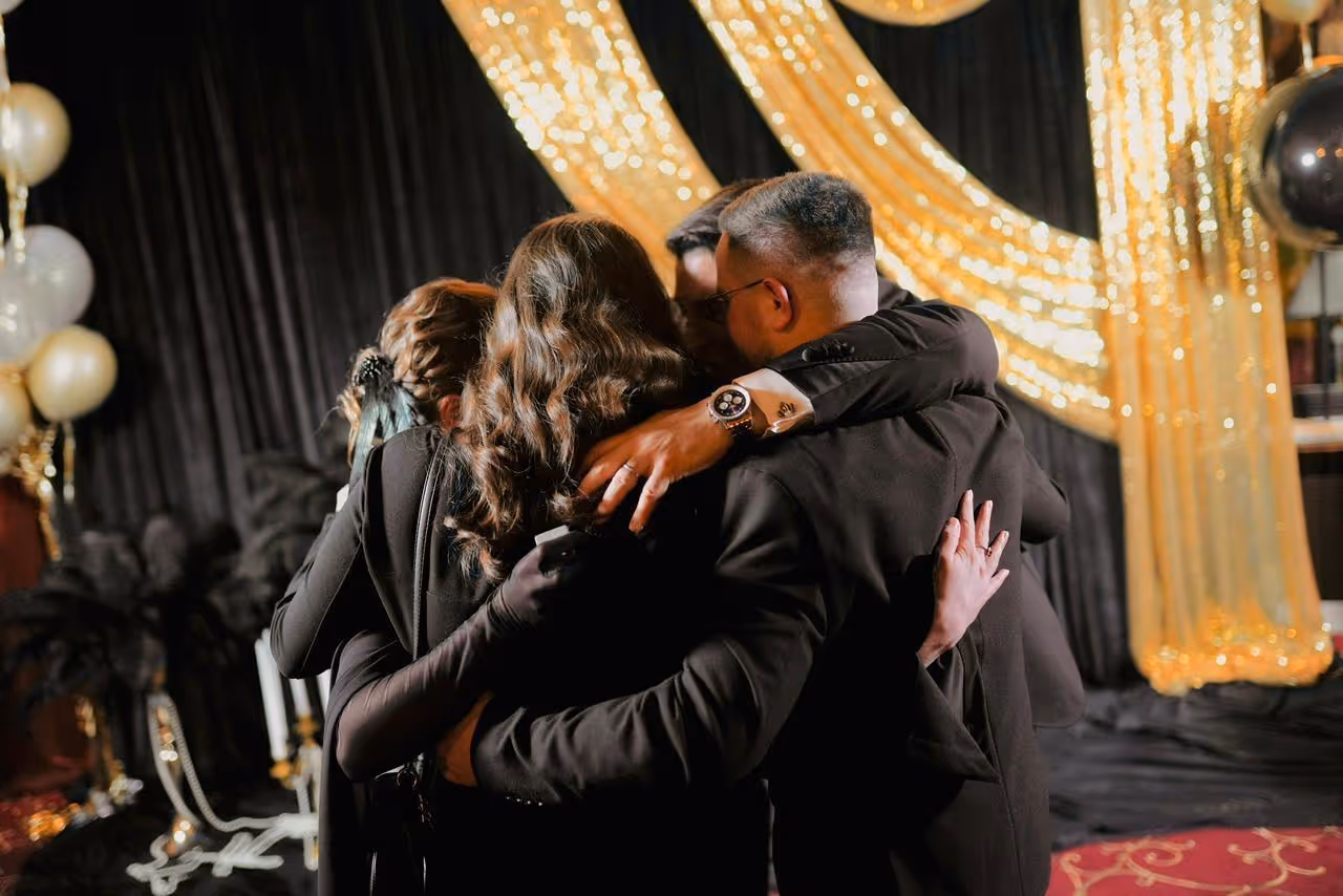 A group embracing beneath gold lights at an event.